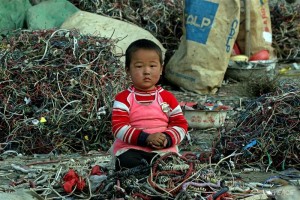 A small Chinese child sitting among cables and e-waste, Guiyu, China. Much of modern electronic equipment contains toxic ingredients. Vast amounts are routinely and often illegally shipped as waste from Europe, USA and Japan to countries in Asia as it is easier and cheaper to dump the problem on poorer countries with lower environmental standards. This practise exposes the workers and communities involved in dismantling e-waste to serious, environmental problems, danger and health hazards. Greenpeace is strongly urging major manufactures to exclude toxic materials from their products.